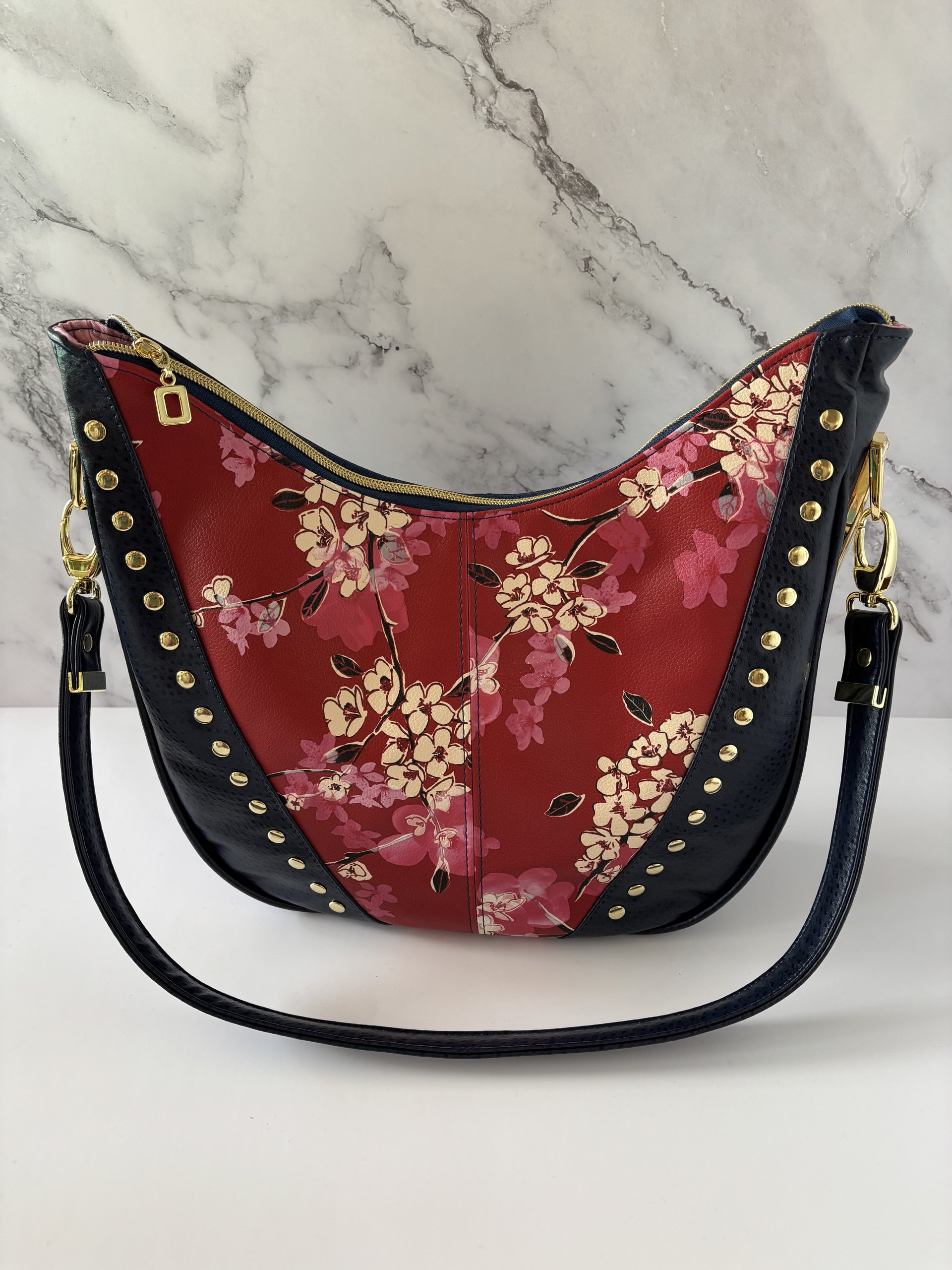 Curved semi-slouchy handbag with matching eyewear/sunglass case, in a floral pattern in cream, pink, and maroon tones, with a rich solid navy